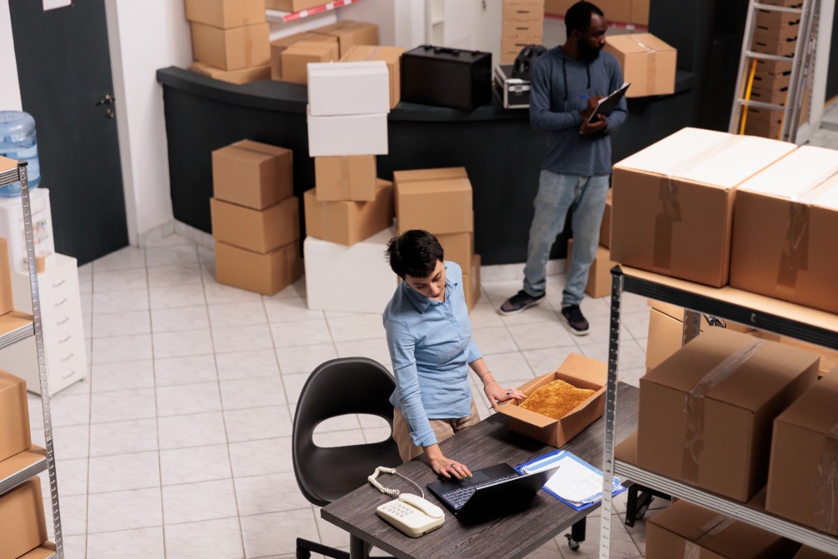 top-view-warehouse-supervisor-packing-client-clothes-order-cardboard-box-while-checking-shipping-details-laptop-computer-team-working-storehouse-delivery-department (1)